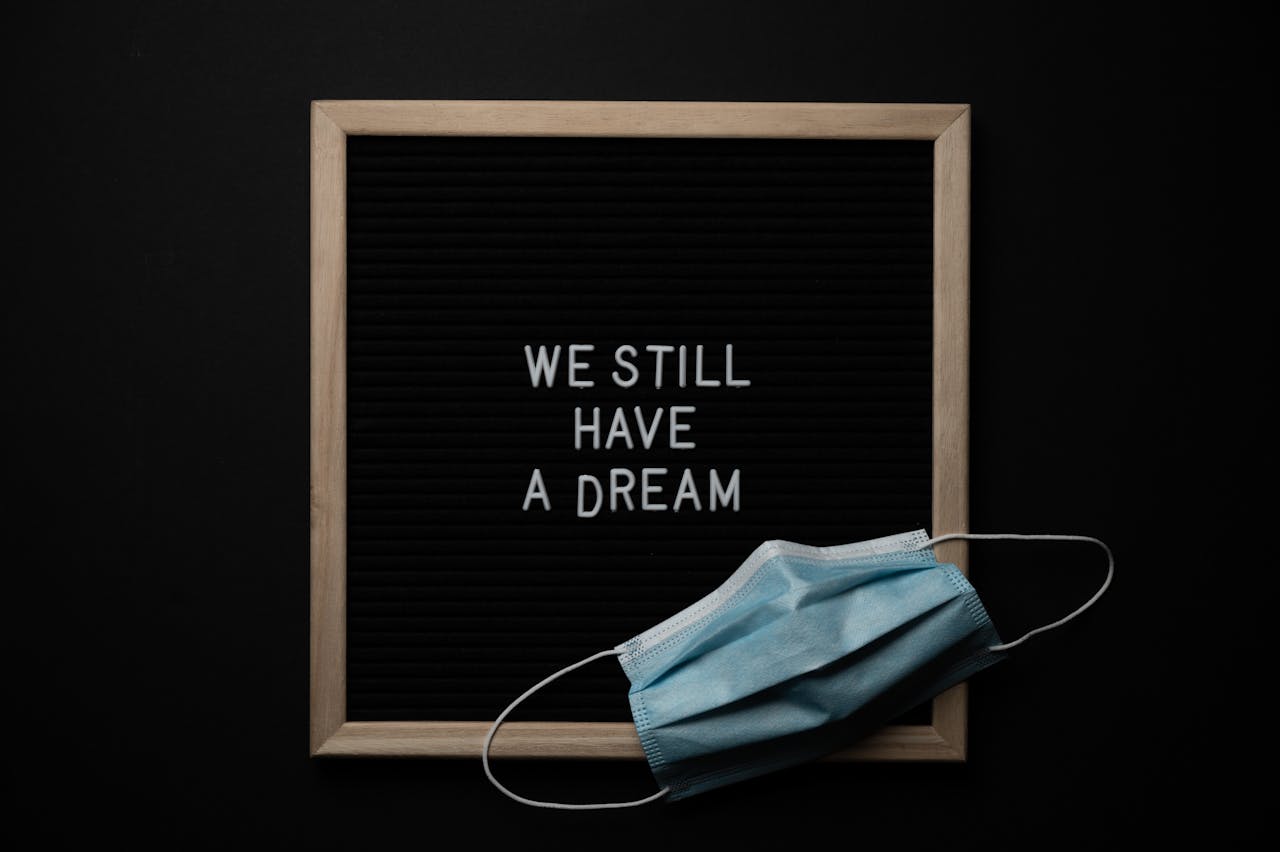 Blackboard with wooden frame with white We Still Have a Dream inscription and medical mask placed on black background